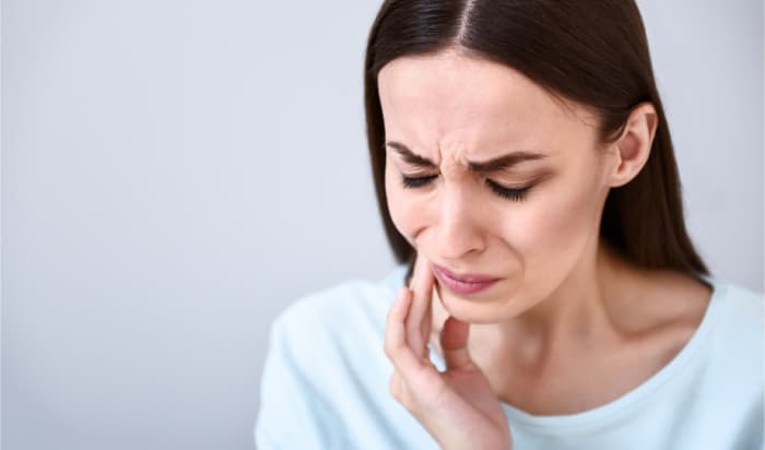 Brown-haired woman cringes in pain as she puts her hand up to her cheek